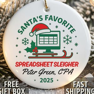 May include: White ceramic Christmas ornament with a gold string for hanging. The ornament features the text "SANTA'S FAVORITE" and "SPREADSHEET SLEIGHER" in green and red, along with a graphic of a computer monitor with a Santa hat.