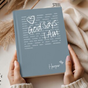 Peut inclure: Un journal bleu acier avec les mots "God Says I Am" en &eacute;criture blanche. Le journal a un c&oelig;ur et le nom "Harper" sur la couverture. Le journal est tenu dans deux mains.