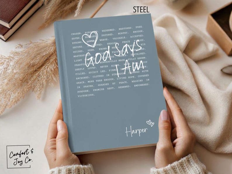 Peut inclure: Un journal bleu acier avec les mots "God Says I Am" en &eacute;criture blanche. Le journal a un c&oelig;ur et le nom "Harper" sur la couverture. Le journal est tenu dans deux mains.