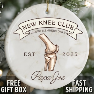 May include: Round ceramic Christmas ornament with a marble effect. The ornament features the text "NEW KNEE CLUB" and a drawing of a knee joint. Below the drawing is the name "Papa Joe" and the year "2025".