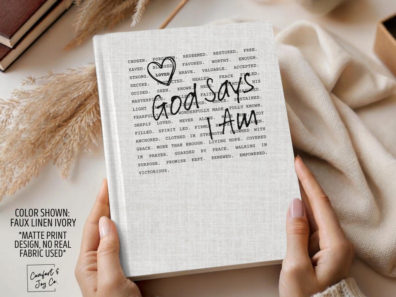 Peut inclure: Journal ivoire avec l'inscription "God Says I Am" dans une police manuscrite. La couverture pr&eacute;sente un motif imprim&eacute; mat et une texture en faux lin. Les mots "Chosen, Saved, Strong, Loved" sont imprim&eacute;s autour du texte principal.
