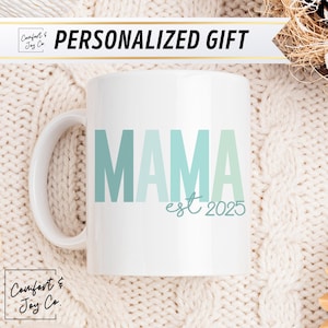May include: White ceramic mug with a blue and green ombre design that says "MAMA est 2025".