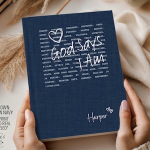 Peut inclure: Journal bleu marine avec le texte "God says I Am" &eacute;crit dans une police manuscrite. Le journal a une texture de faux lin et le nom "Harper" est &eacute;crit en bas. Le journal est tenu par une personne.