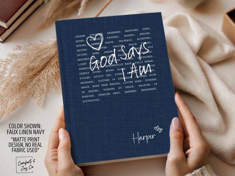 Peut inclure: Journal bleu marine avec le texte "God says I Am" &eacute;crit dans une police manuscrite. Le journal a une texture de faux lin et le nom "Harper" est &eacute;crit en bas. Le journal est tenu par une personne.