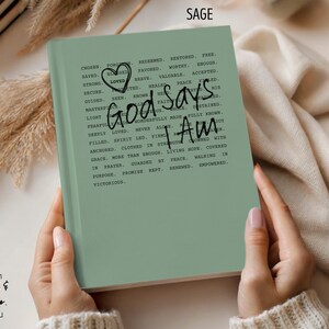Peut inclure: Journal vert sauge avec l'inscription "God Says I Am" et d'autres affirmations positives. Le journal comporte un gribouillage de c&oelig;ur et est ouvert, montrant le texte. Le journal fait partie de la collection Comfort & Joy Co.