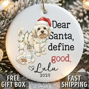 May include: White ceramic Christmas ornament with a dog wearing a Santa hat and Christmas lights. Text reads "Dear Santa, define good. Lulu 2025." Includes a plate of cookies and a glass of milk. Gold hanging cord.