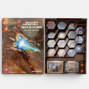 Könnte beinhalten: Space Empires Replicators Erweiterungs-Spielschachtel und offenes Inlay. Der Deckel zeigt eine Raumschiff-Illustration und Text. Das Inlay enthält sechseckige Plättchen, zwei Kartendecks und orangefarbene Würfel in einer braunen Kunststoffeinlage.