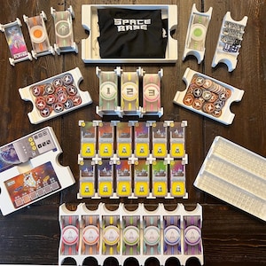 May include: A white plastic organiser with compartments for storing game pieces and cards. The organiser has a label that says "Space Base".