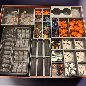 May include: A brown and orange game organizer with multiple compartments for storing game pieces. The organizer has a variety of compartments for storing different sized pieces, including dice, cards, and tokens.