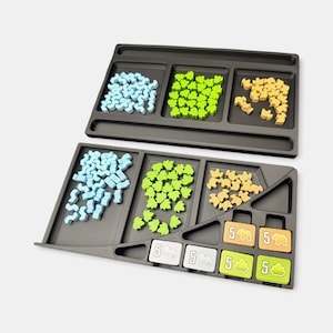 K&ouml;nnte beinhalten: Zwei schwarze Brettspiel-Organizer aus Kunststoff mit F&auml;chern. Das obere Fach enth&auml;lt hellblaue, lindgr&uuml;ne und hellbraune Holzspielsteine. Das untere Fach enth&auml;lt &auml;hnliche Spielsteine sowie vier quadratische Pl&auml;ttchen mit der Zahl 5.