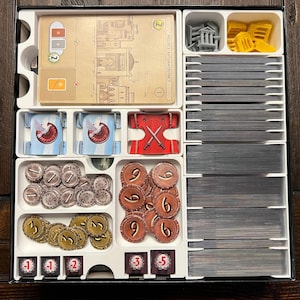 Op de afbeelding: Een witte plastic organizer met vakken om spelstukken en kaarten op te bergen. De organizer heeft een label met de tekst "Pocket Mithian District". De vakken bevatten verschillende spelstukken, waaronder tokens, kaarten en dobbelstenen.