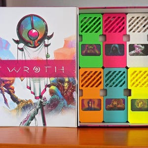 以下が含まれることがあります： 「WROTH」の文字が表紙に書かれた、開いたボードゲームの箱。箱には、ゲームの駒が入ったカラフルなコンパートメントがあります。ゲームの駒は、緑、ピンク、黄色などの明るい色です。箱は木製の表面に置かれています。