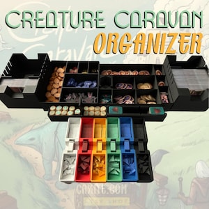 May include: Creature Caravan board game organizer with compartments for cards, tokens, and dice. The organizer is made of black plastic and has a variety of colored compartments. The organizer is labeled "Creature Caravan Organizer".
