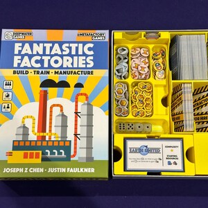 May include: A yellow and white box with a game insert. The box features a colourful illustration of a factory with the text "Fantastic Factories" and "Build - Train - Manufacture". The game insert has compartments for game pieces, cards, and dice.