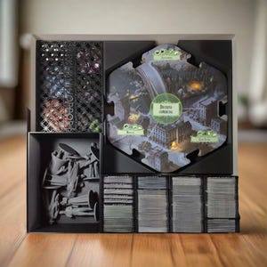 Puede incluir: Un organizador negro con compartimentos para guardar piezas de juegos de mesa. El organizador tiene una ficha hexagonal de juego de mesa con un diseño de mapa de ciudad, un compartimento con figuras en miniatura y un compartimento con barajas de cartas.