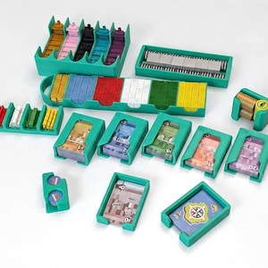 Puede incluir: Un conjunto organizador para juegos de mesa con bandejas y soportes de plástico color verde azulado. Incluye varios recipientes llenos de pequeños cubos de madera de colores, mazos de cartas, billetes de juego y fichas circulares variadas.