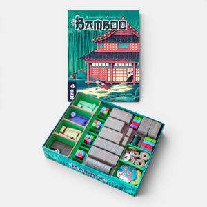 Peut inclure: Le jeu de société Bamboo présente un couvercle de boîte illustré d'un bâtiment de style japonais et d'une forêt. La boîte ouverte contient un insert en plastique avec des compartiments organisés contenant des cartes, des cubes en bois et des jetons.