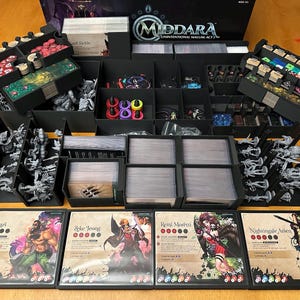 Può includere: Un organizer nero per il gioco da tavolo Middara, con vari scomparti contenenti pezzi di gioco, carte e miniature. La scatola del gioco è visibile sullo sfondo, insieme a carte personaggio con illustrazioni e nomi come Rook Lars e Zeke Jeong.