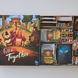 Op de afbeelding: Bordspel "Flock Together" met een illustratie van antropomorfe dieren in een bos. De open doos toont spelcomponenten, waaronder kaarten, fiches en spelstukken, netjes georganiseerd in compartimenten.