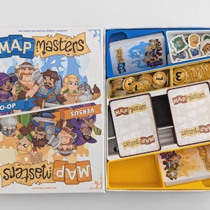 以下が含まれることがあります： Map Mastersボードゲームセット。白い箱の蓋にはキャラクターのイラストと「Map Masters」「Co-Op」「Versus」の文字が描かれています。開いた箱の中には、青、黄、白のプラスチック製トレイがあり、カードデッキと丸いトークンが収納されています。