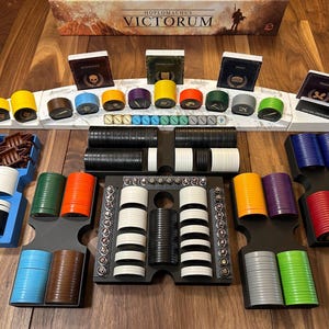 Puede incluir: Un tablero de juego con fichas y cartas de varios colores. El tablero de juego está hecho de madera y tiene un diseño en blanco y negro. Las fichas están en pilas de diferentes alturas y están dispuestas en una cuadrícula. Las cartas están en una fila en la parte superior del tablero y tienen una variedad de imágenes en ellas. El juego se llama "Hoplomachus Victorum".