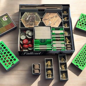 Könnte beinhalten: Ein grüner und grauer Organizer für das Brettspiel Fallout. Der Organizer enthält Fächer für Karten, Spielsteine und Miniaturen. Der Organizer ist aus hochwertigen Materialien gefertigt und wurde so konzipiert, dass er perfekt in die Fallout-Spielbox passt.