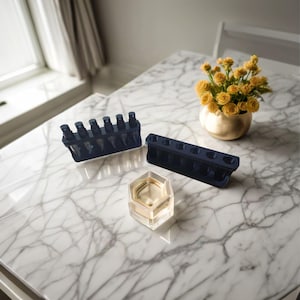 May include: Two black plastic organizers for perfume bottles. One organizer holds seven bottles and the other holds eight bottles. The organizers are on a white marble surface with a small glass dish and a bouquet of yellow flowers in a gold vase.