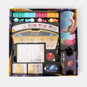 K&ouml;nnte beinhalten: Ein Brettspiel-Boxeinsatz mit verschiedenen Spielkomponenten, darunter bunte Holzspielsteine, ein gro&szlig;es zentrales Spielerbrett mit numerischen Symbolen, Stapel rechteckiger Karten, ein runder roter Spielstein und ein sechseckiges blaues Planetenpl&auml;ttchen.