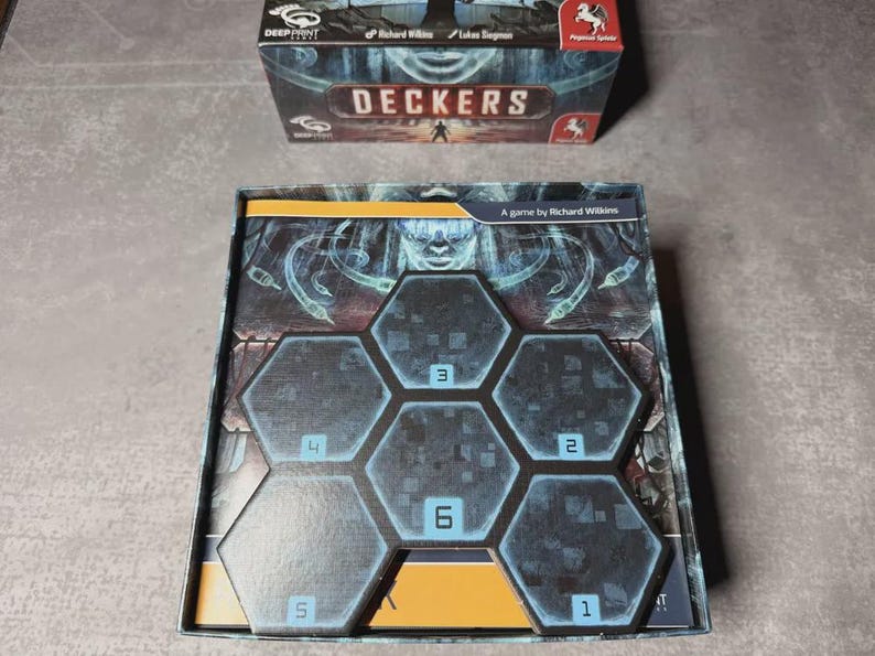 May include: A board game box and game board with a dark, futuristic theme. The box reads "DECKERS" and the game board features hexagonal tiles numbered 1 to 6. The game is by Richard Wilkins.