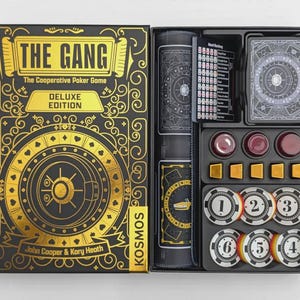 Puede incluir: Juego de póquer cooperativo The Gang Deluxe Edition en una caja negra y dorada con diseño de caja fuerte. La caja abierta contiene un tapete de juego enrollado, una baraja de cartas, una tarjeta de referencia, tres fichas rojas, cinco cubos dorados y seis fichas numeradas.