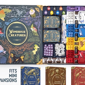 Op de afbeelding: Een bordspeldoos getiteld Wondrous Creatures met een open interieur met georganiseerde spelonderdelen, waaronder kaartspellen, fiches en gekleurde bakjes. Hieronder staan drie kleinere boekvormige dozen met de labels Gargantuan Beasts, Upgraded Components en Crew Set, met de tekst Fits Mini Expansions.