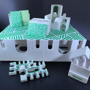 Op de afbeelding: Witte opbergdozen en accessoires met een groen geometrisch ontwerp. De dozen hebben een witte basis met een groen diagonaal lijnenpatroon. Er zijn ook extra witte accessoires met groene accenten. Het woord "Rocks" staat op een van de accessoires.