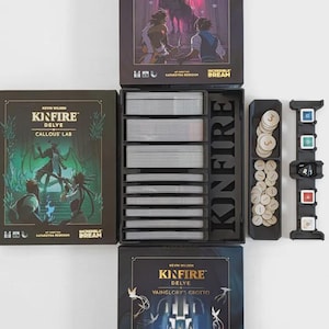 Może przedstawiać: Zestaw gier planszowych z trzema pudełkami, stosami kart i elementami gry. Pudełka zawierają ilustracje i tekst, w tym "KINFIRE DELVE" i "INCREDIBLE DREAM". Zestaw zawiera czarny organizer z przegródkami na karty i tacę na żetony i kości.
