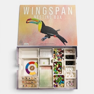 Op de afbeelding: Wingspan Nesting Box bordspel. De doos toont een illustratie van een toekan. Binnenin bevat het spel verschillende componenten zoals dobbelstenen, kaarten en kleurrijke eivormige spelstukken. Het spel is ontworpen door Elizabeth Hargrave.