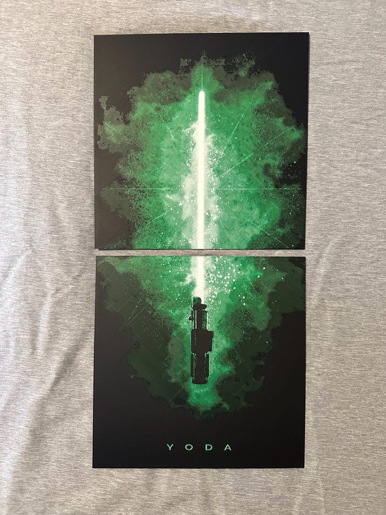 K&ouml;nnte beinhalten: Zwei schwarze Kunstdrucke mit einem gr&uuml;nen Lichtschwert-Design. Einer zeigt den Lichtstrahl, der andere den Griff, mit dem Wort "YODA" unten. Der Hintergrund hat einen gr&uuml;nen, rauchigen Effekt. F&uuml;r Star Wars-Fans.