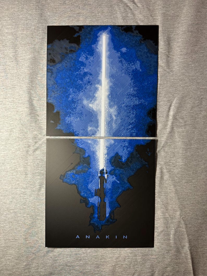 K&ouml;nnte beinhalten: Zweiteiliges Kunstwerk mit einem blau-wei&szlig;en Lichtschwert-Design. Das Lichtschwert hat eine leuchtend wei&szlig;e Klinge vor einem blau-schwarzen Hintergrund. Der Name "ANAKIN" ist unten in Wei&szlig; aufgedruckt.