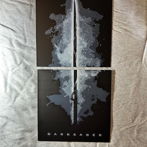 K&ouml;nnte beinhalten: Zwei schwarze rechteckige Kunstdrucke mit einer stilisierten Illustration des Darksaber. Das Kunstwerk zeigt das Lichtschwert mit wei&szlig;en und grauen Akzenten vor einem dunklen Hintergrund. Das Wort "DARKSABER" ist unten aufgedruckt.