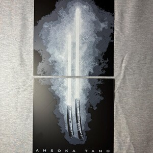 K&ouml;nnte beinhalten: Zweiteiliges Kunstwerk mit wei&szlig;en Lichtschwertern vor einem rauchigen, grauen Hintergrund. Das untere Feld zeigt den Text "AHSOKA TANO" in wei&szlig;en Gro&szlig;buchstaben. Das Kunstwerk hat eine dunkle, dramatische &Auml;sthetik, wobei der Fokus auf dem hellen Gl&uuml;hen der Lichtschwerter liegt.