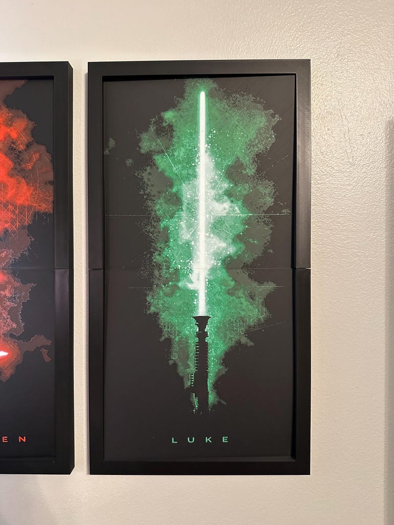 K&ouml;nnte beinhalten: Gerahmter Kunstdruck mit einem gr&uuml;nen Lichtschwert-Design, einer wei&szlig;en Klinge und gr&uuml;nen Energieausbr&uuml;chen auf schwarzem Hintergrund. Der Name "LUKE" ist unten in Wei&szlig; gedruckt. Das Kunstwerk befindet sich in einem schwarzen Rahmen.