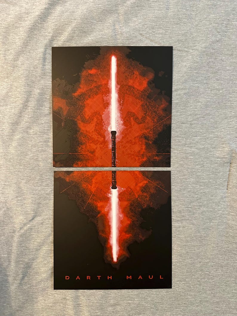 K&ouml;nnte beinhalten: Zweiteiliger Kunstdruck mit einem rot-wei&szlig;en Lichtschwert-Design vor dunklem Hintergrund. Die Worte "DARTH MAUL" sind unten auf dem Druck in Wei&szlig; gedruckt. Das Lichtschwert ist zwischen den beiden Teilen geteilt.