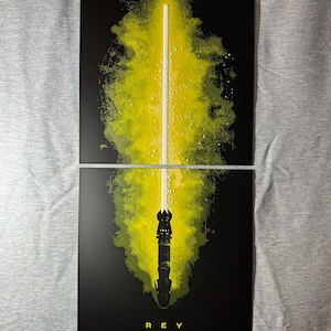 K&ouml;nnte beinhalten: Zweiteiliges Kunstwerk mit einem gelben Lichtschwert vor schwarzem Hintergrund. Die Klinge des Lichtschwerts ist wei&szlig;, mit einem gelben und gr&uuml;nen Spritzeffekt. Das Wort "REY" ist unten in Wei&szlig; gedruckt.