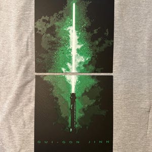 K&ouml;nnte beinhalten: Zweiteilige Grafik mit einem gr&uuml;nen Lichtschwert-Design vor schwarzem Hintergrund. Das Lichtschwert hat eine leuchtend gr&uuml;ne Klinge und einen detaillierten Griff. Der Text "QUI-GON JINN" ist unten in Wei&szlig; gedruckt.
