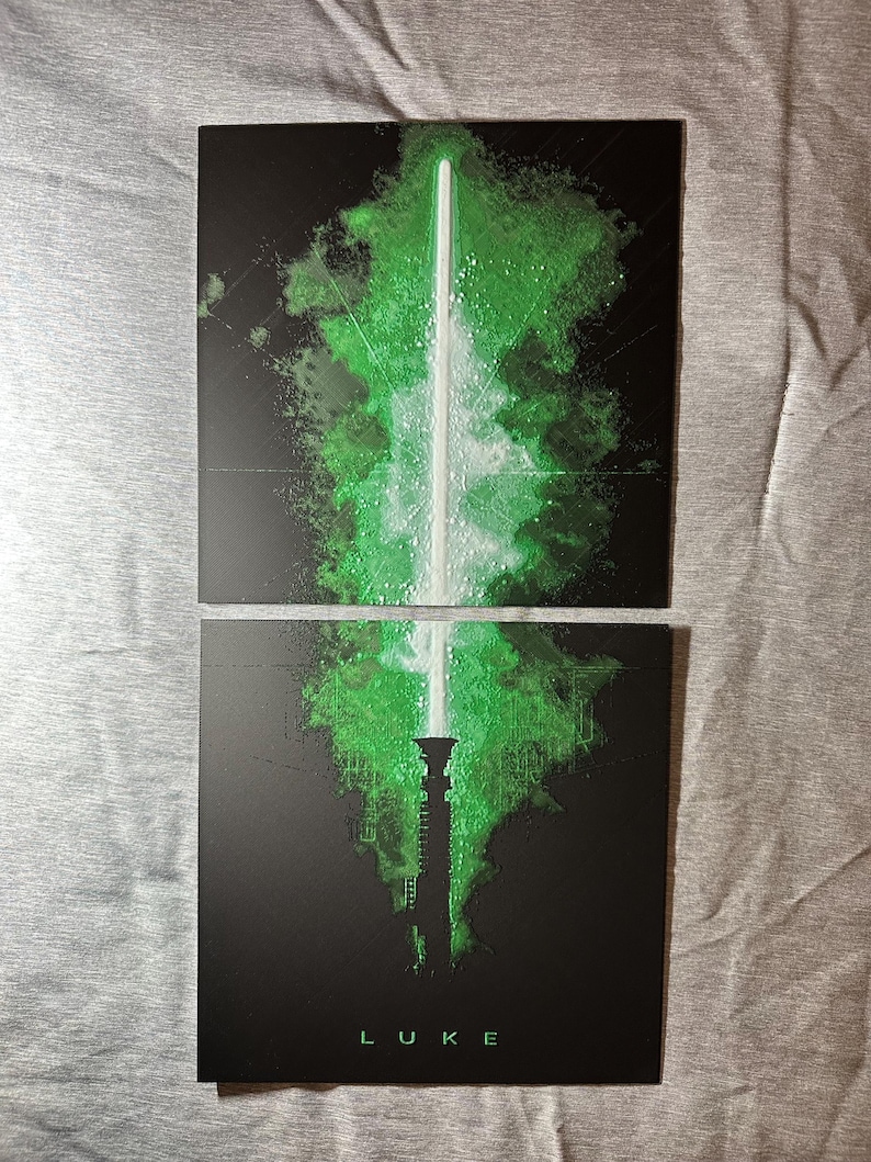 K&ouml;nnte beinhalten: Zweiteiliger Kunstdruck mit einem gr&uuml;nen Lichtschwert-Design auf schwarzem Hintergrund. Die Lichtschwertklinge ist wei&szlig;, mit einem gr&uuml;nen, strukturierten Effekt. Das Wort "LUKE" ist unten gr&uuml;n gedruckt.