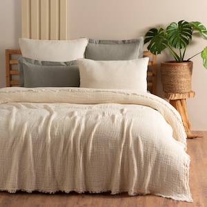 May include: A white waffle-weave throw blanket with a fringed edge, folded on a bed with a white and gray pillow arrangement.