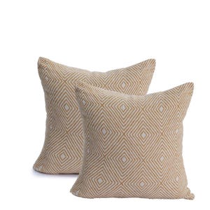 May include: Two square decorative pillows with a geometric diamond pattern. The pillows are a light beige color with a white diamond pattern. The pillows are made of a textured fabric.