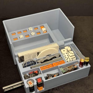 May include: A gray, multi-compartment game organizer with orange accents. It contains dice, cards, and miniature game pieces. The organizer is designed to hold various game components, keeping them organized and accessible.