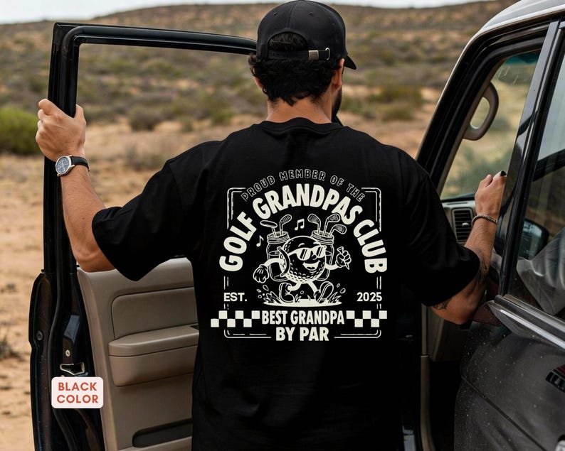 May include: Black t-shirt with a white graphic that reads "Proud Member of the Golf Grandpas Club." The graphic features a golf ball character with sunglasses, golf clubs, and the text "Best Grandpa by Par." The shirt also has the text "Est. 2025."