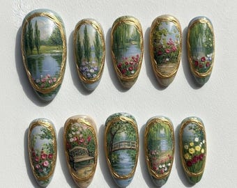 May include: A set of ten oval-shaped artificial nails, each hand-painted with a miniature landscape scene. The designs feature serene waterscapes with trees, flowers, and a bridge, framed by a gold border. The nails are a light blue color.