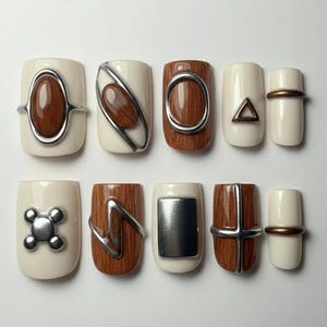 May include: A set of ten press-on nails in various designs. Some nails are off-white with silver or brown accents, while others feature a wood grain pattern. The nails have geometric shapes and metallic details.