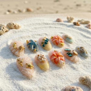May include: A collection of ten artificial nails, each adorned with unique, beach-themed embellishments. Designs include seahorses, starfish, and floral accents, set against a backdrop of white sand. The nails feature a variety of colors, including pink, blue, and gold.